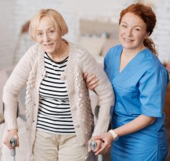 red-haired woman in scrubs supports older woman using crutches